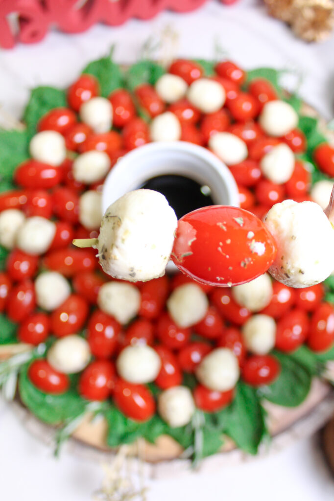a Caprese skewer in front of a Christmas Caprese wreath salad