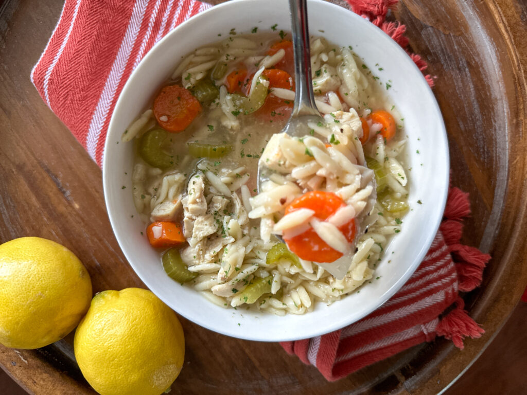 lemon chicken orzo soup in a white bowl with lemons to the left