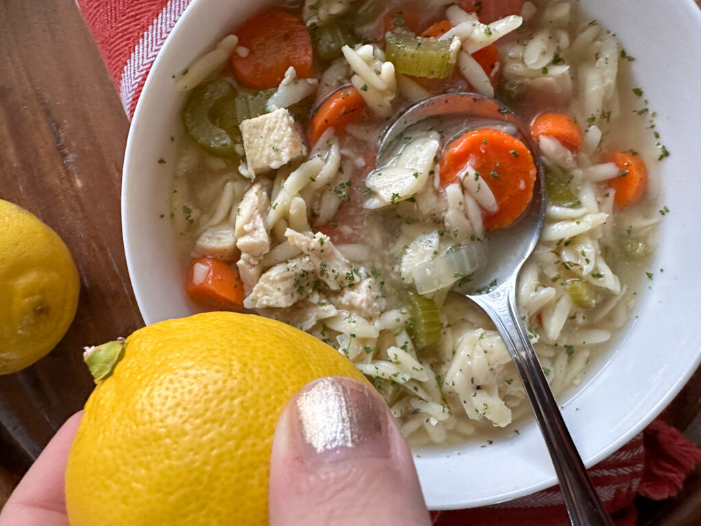 chicken lemon orzo soup in a pot with a woman holding a lemon on top