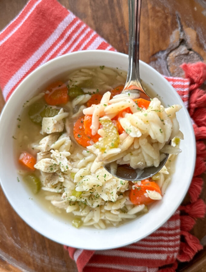 lemon orzo soup with chicken in a white bowl with a silver spoon