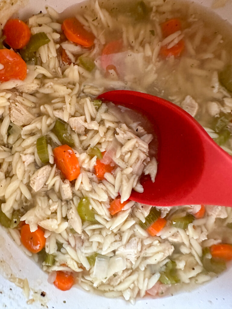 lemon chicken orzo soup in pot with red spoon