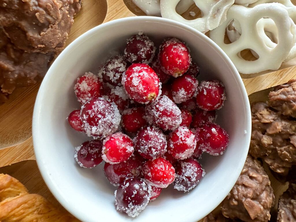 sugared cranberries in white bowl on dessert board
