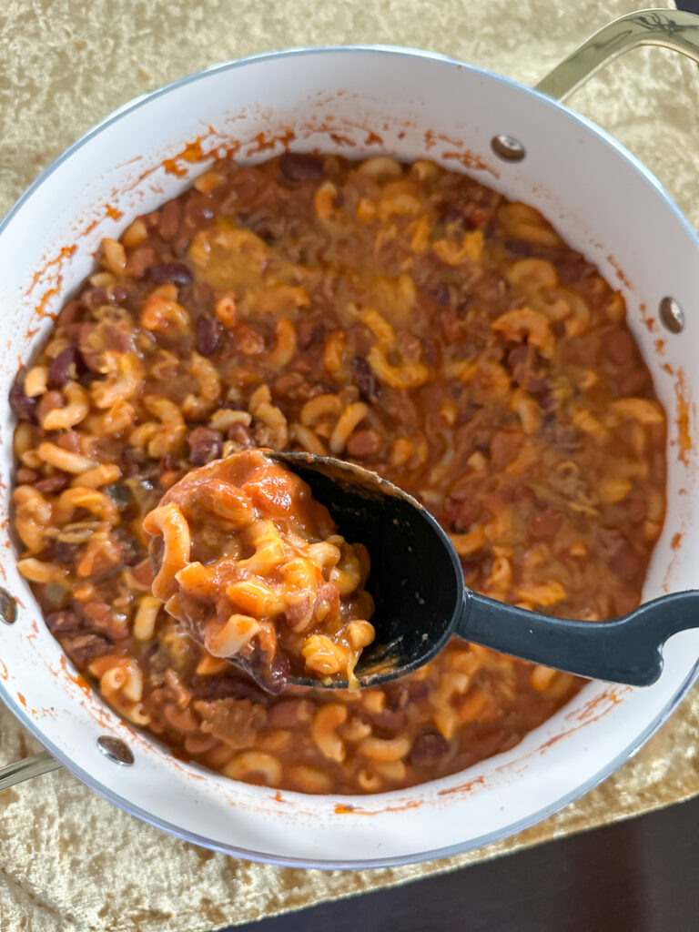 leftover chili mac on serving spoon above pan