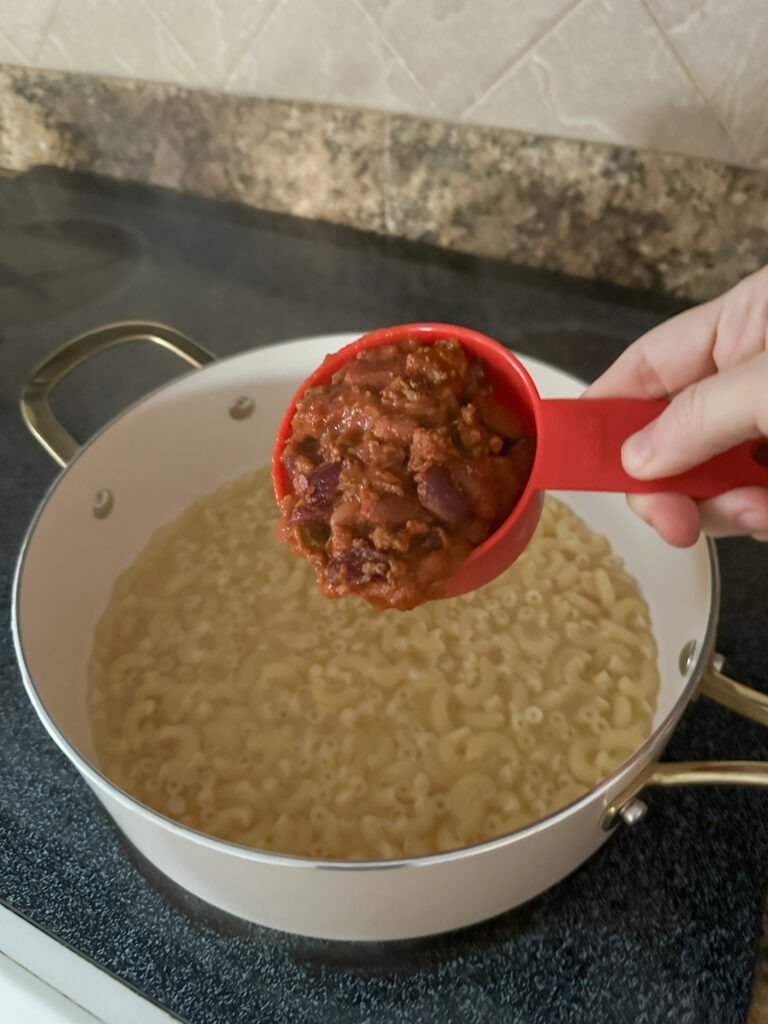 woman adds leftover chili to macaroni  in white pot