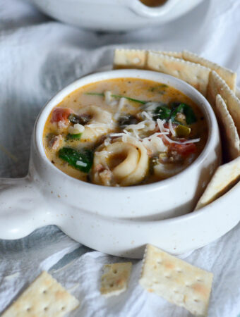 sausage spinach tortellini soup in a white bowl with crackers