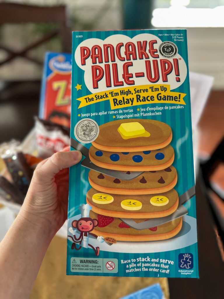 woman holds Pancake Pile-Up game in her hand to give in a snow day box gift during a snow storm