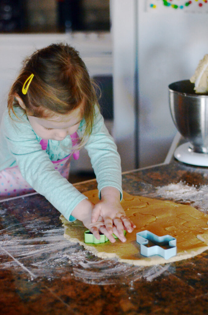 little girl cutting cross cookies with cookie cutters