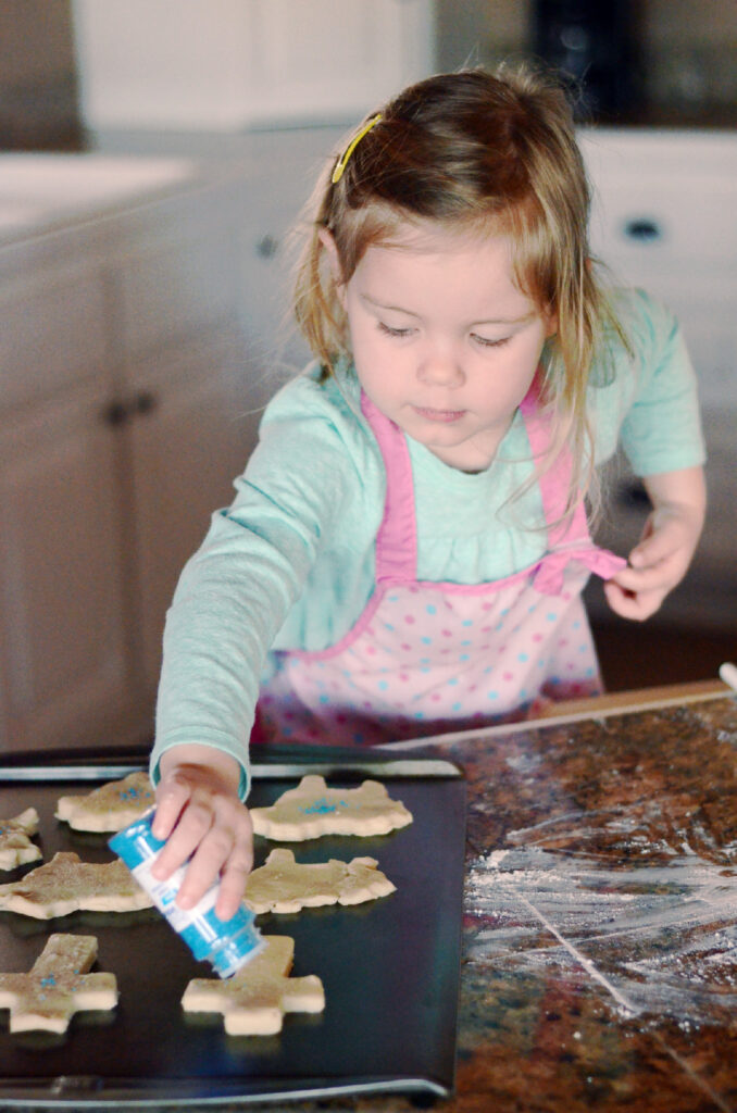 little girl shakes blue sprinkles onto Easter cross cookies