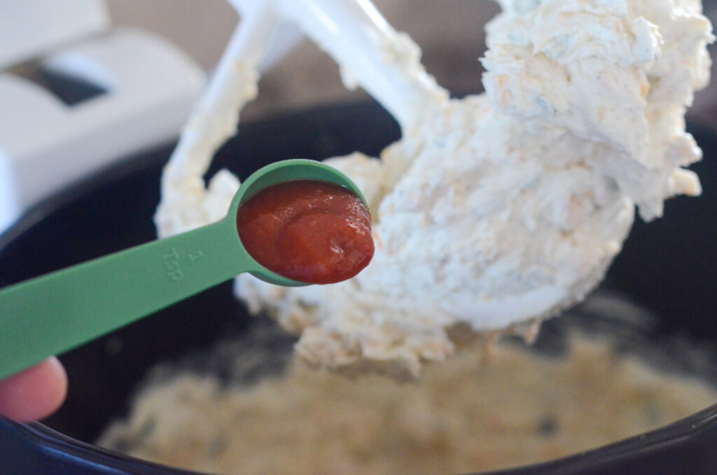 spicy Sriracha going into cheese ball mixture in mixing bowl