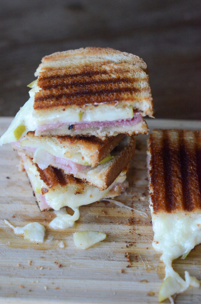 cheese and ham panini sandwich stacked on cutting board