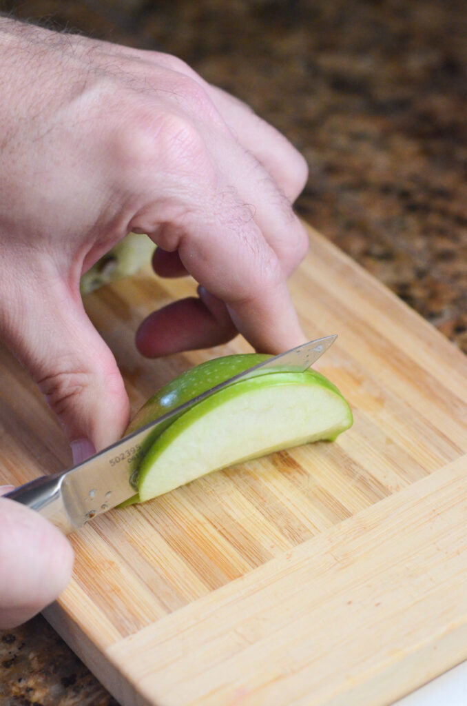 man cuts green apple into thin slices