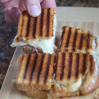man pulls on ham and cheese panini from cutting board