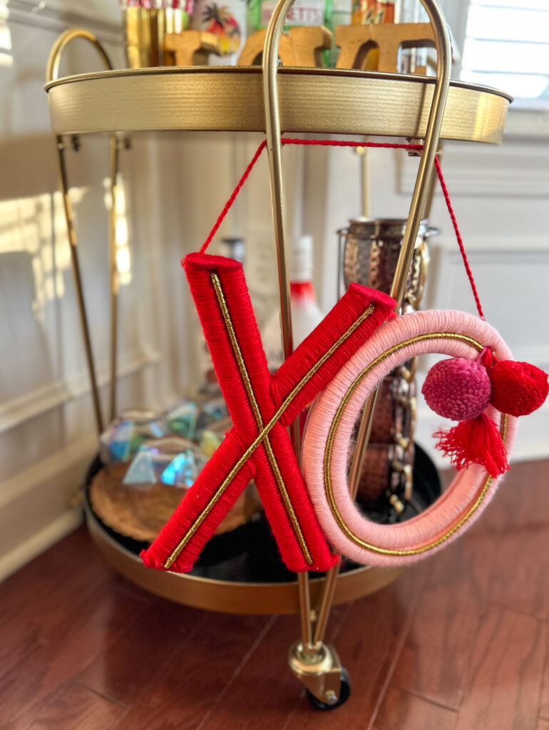 knitted XOXO sign with pom poms hanging on a Valentine's bar cart