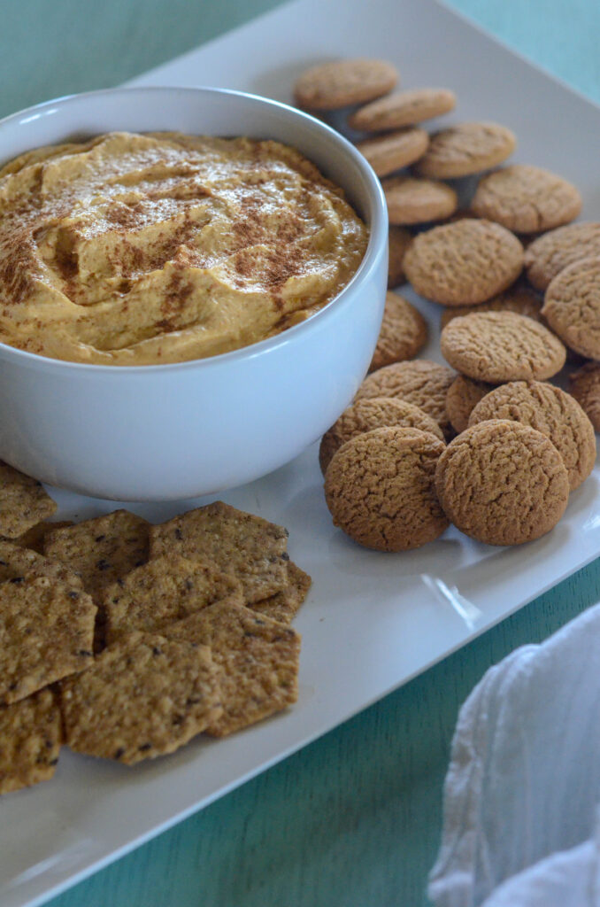 cream cheese pumpkin dip with gingersnaps on a white platter on a blue backdrop