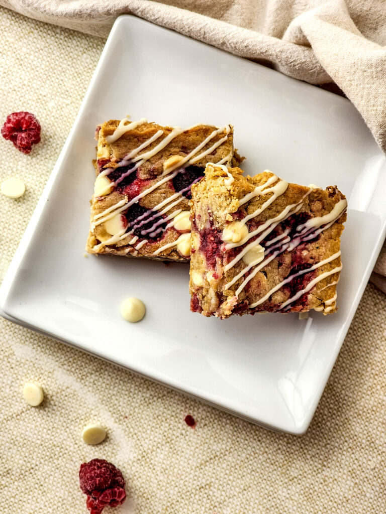 two white chocolate raspberry blondies on a square white plate