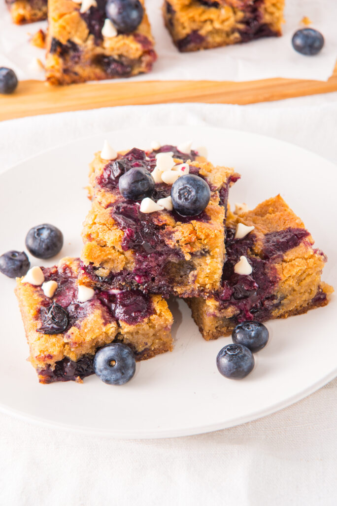 three blueberry white chocolate blondies on a white plate