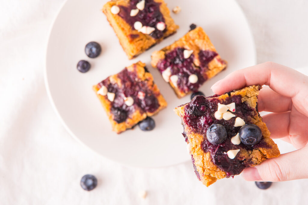 woman holds cut blueberry white chocolate blondies in hand