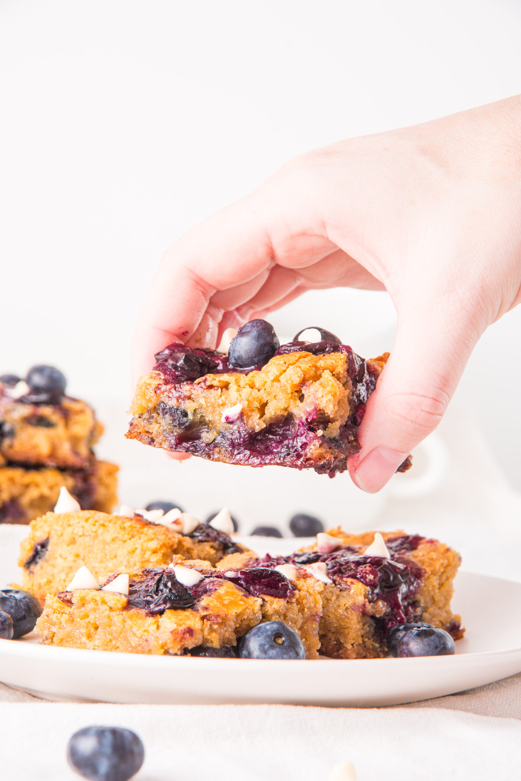 woman lifting blueberry white chocolate blondies from plate