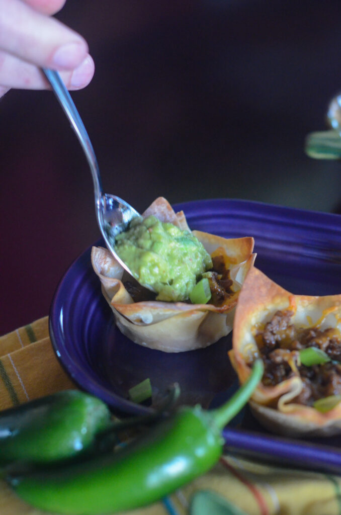 guacamole wonton taco bites with guacamole being spooned on top