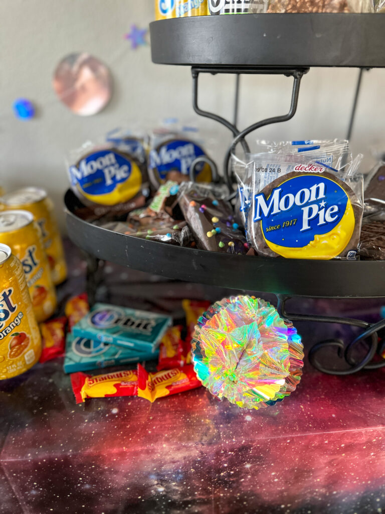 galaxy party food on outer space party table with Moon Pies, Orbit gum, Cosmic brownies, Starburst, and more