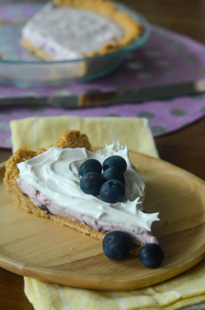blueberry cream cheese pie with graham cracker crust on wooden plate