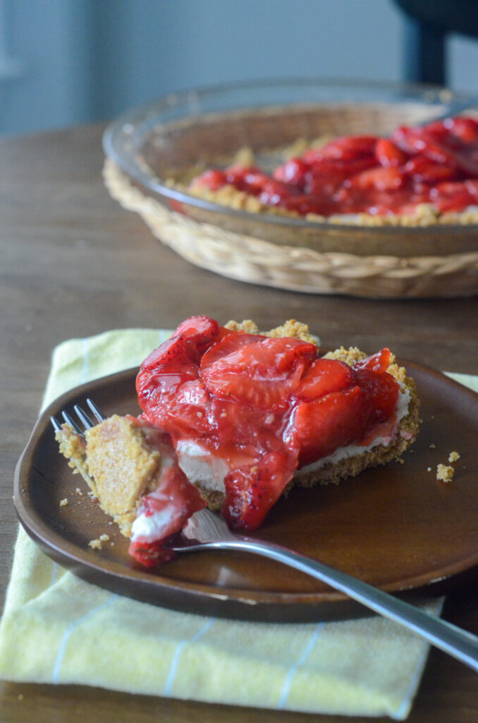 slice of strawberry cream cheese pie on wooden plate with pie plate at back