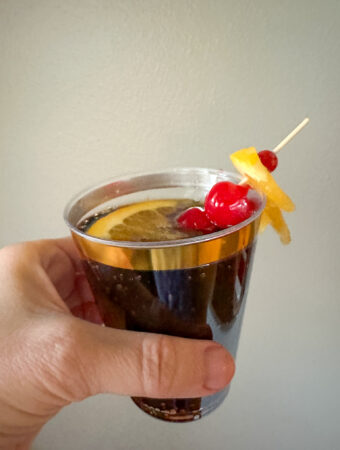 woman holds a Prohibition punch which is a Dr Pepper and rum cocktail drink