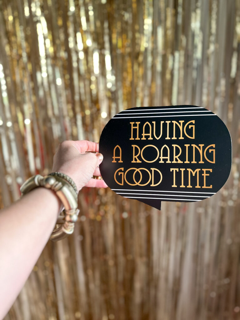 Roaring 20s party sign in woman's hand in front of backdrop