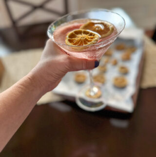 woman holds pink lemonade gin cocktail in martini glass