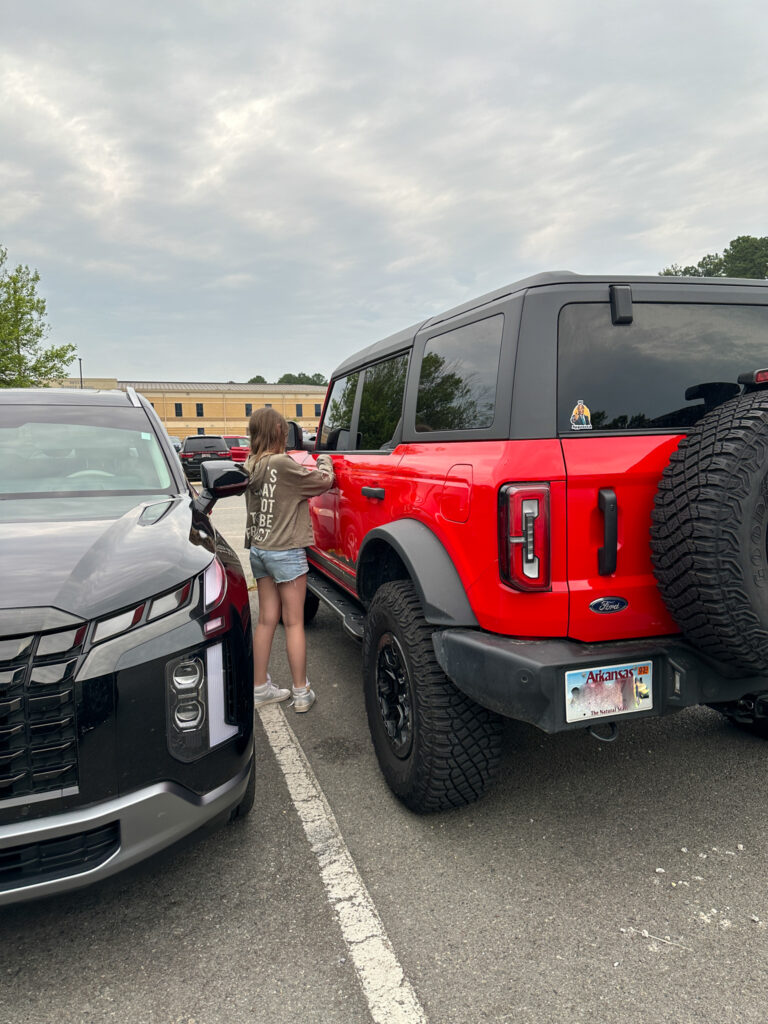 girl placing Buck Buck Bronco cozie gift in door of red Bronco