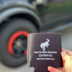 Buck Buck Bronco drink coozie in woman's hand in front of a Ford Bronco