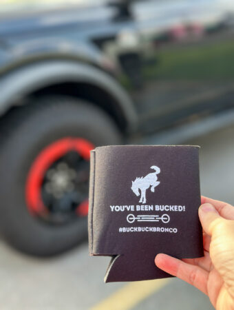 Buck Buck Bronco drink coozie in woman's hand in front of a Ford Bronco