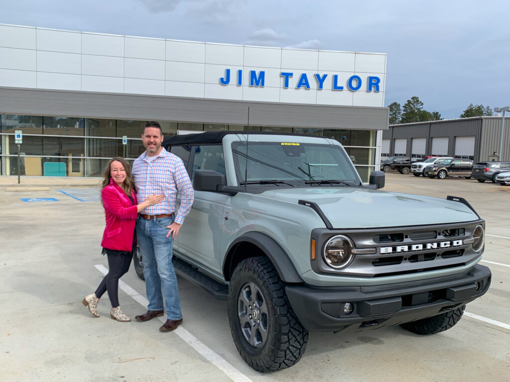 a couple posing with their new Bronco in front of Jim Taylor Ford in Ruston, Louisiana