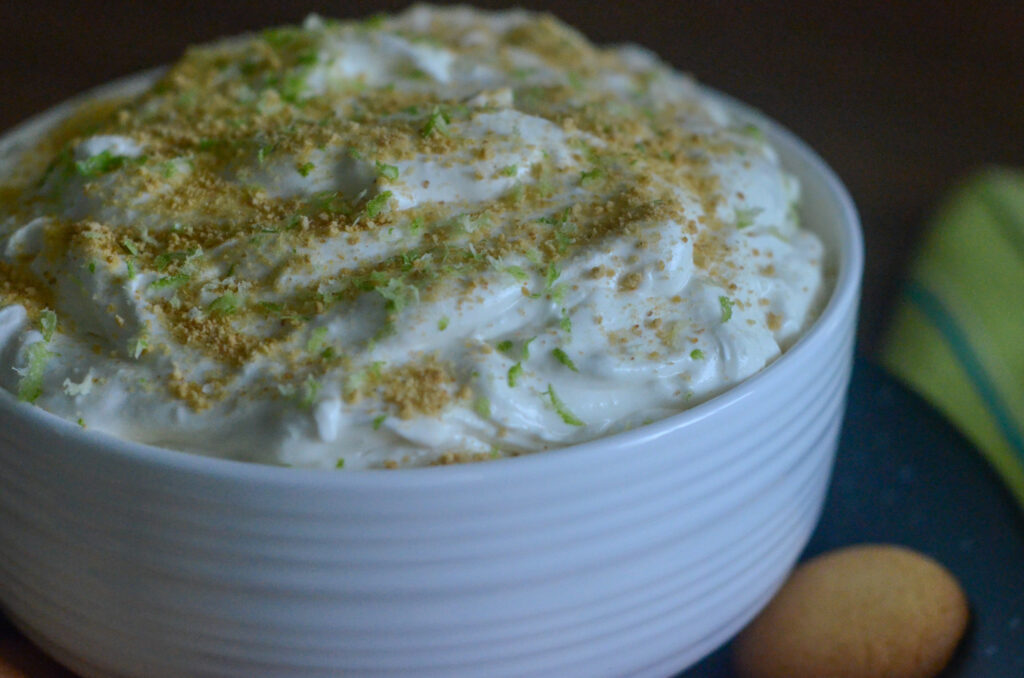 key lime pie dip (also known as no bake key lime cheesecake dip) in a textured white bowl on a black plate