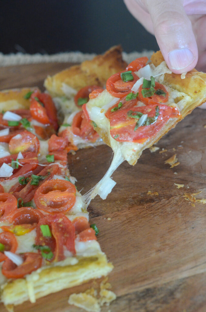 man pulls a piece of warm tomato tart with puff pastry base