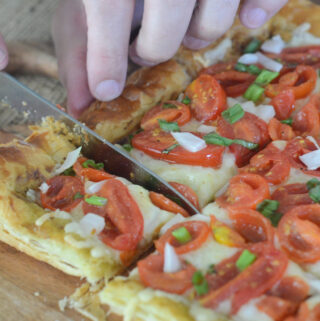 man cuts tomato tart on puff pastry crust