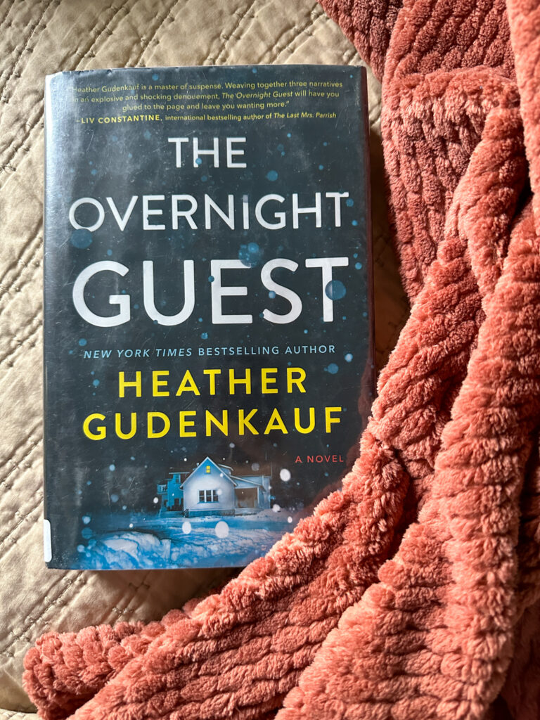 The Overnight Guest beside blanket - winter thrillers to read during a snow storm