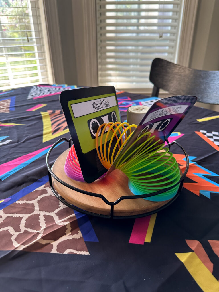 slinky with paper cassette tape cut outs on table with Memphis fashion tablecloth for 1980s party decorations