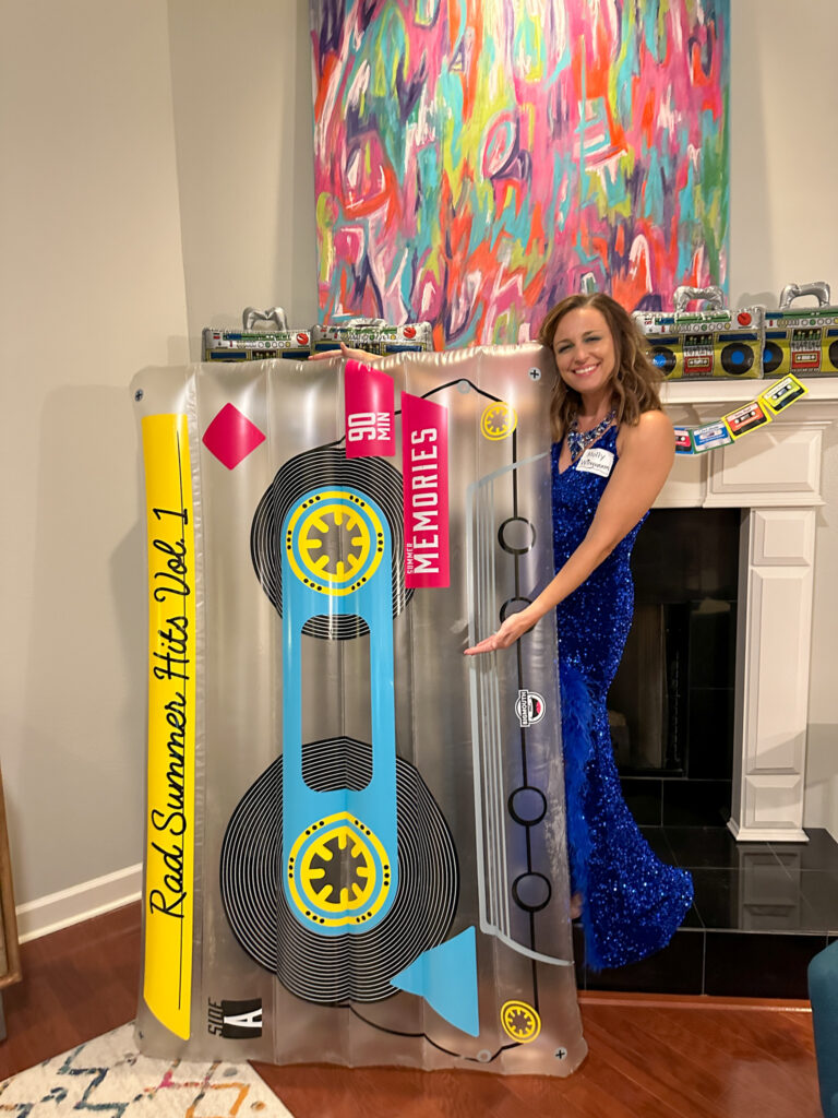 woman stands in front of 1980s mantel with huge cassette tape pool float at a 1980s murder mystery party