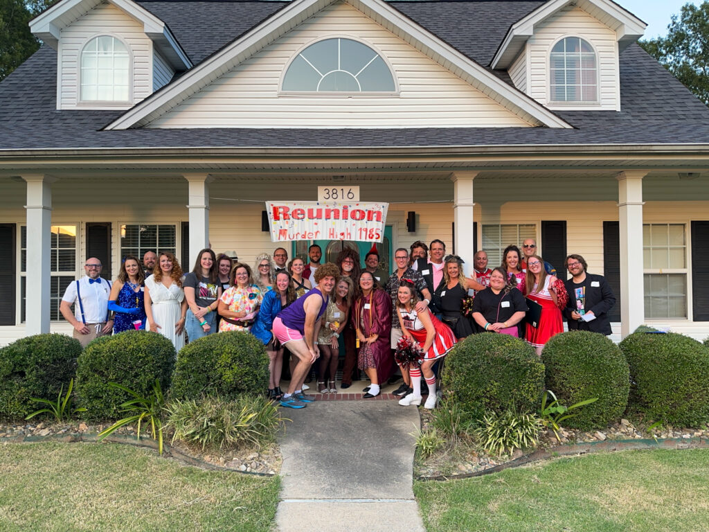 group in 1980s costumes stands under 1980s murder mystery reunion sign