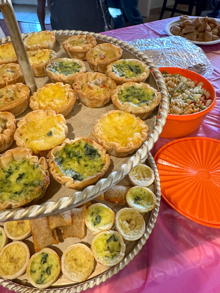 double tier tray of 1980s party food - mini quiche, pizza rolls with Tupperware of pasta salad nearby