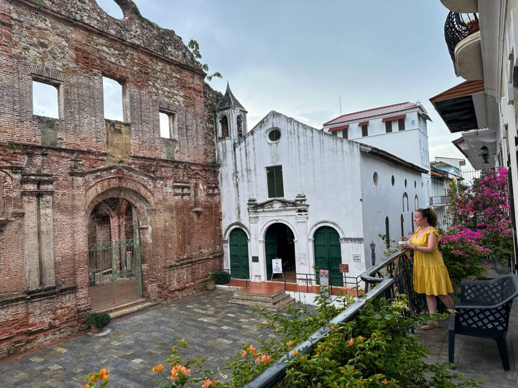 woman stands on apartment balcony in front of Casco Viejo Spanish ruins in Panama City