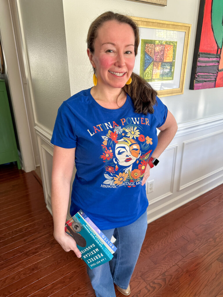 woman wears Latina Power shirt for Hispanic Heritage Month while holding stack of books by Hispanic authors