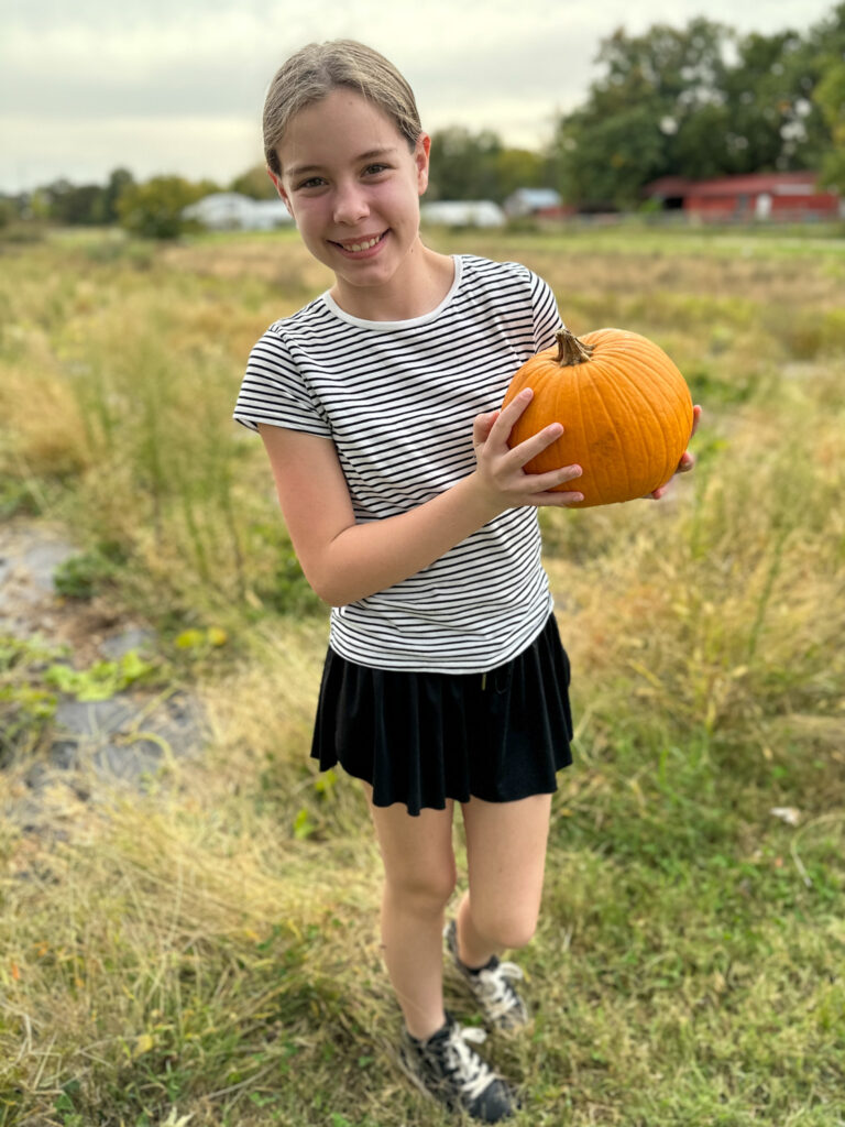 tween Arkansas blogger, Harper, holds pumpkin at Appel Farms during visit to Springdale