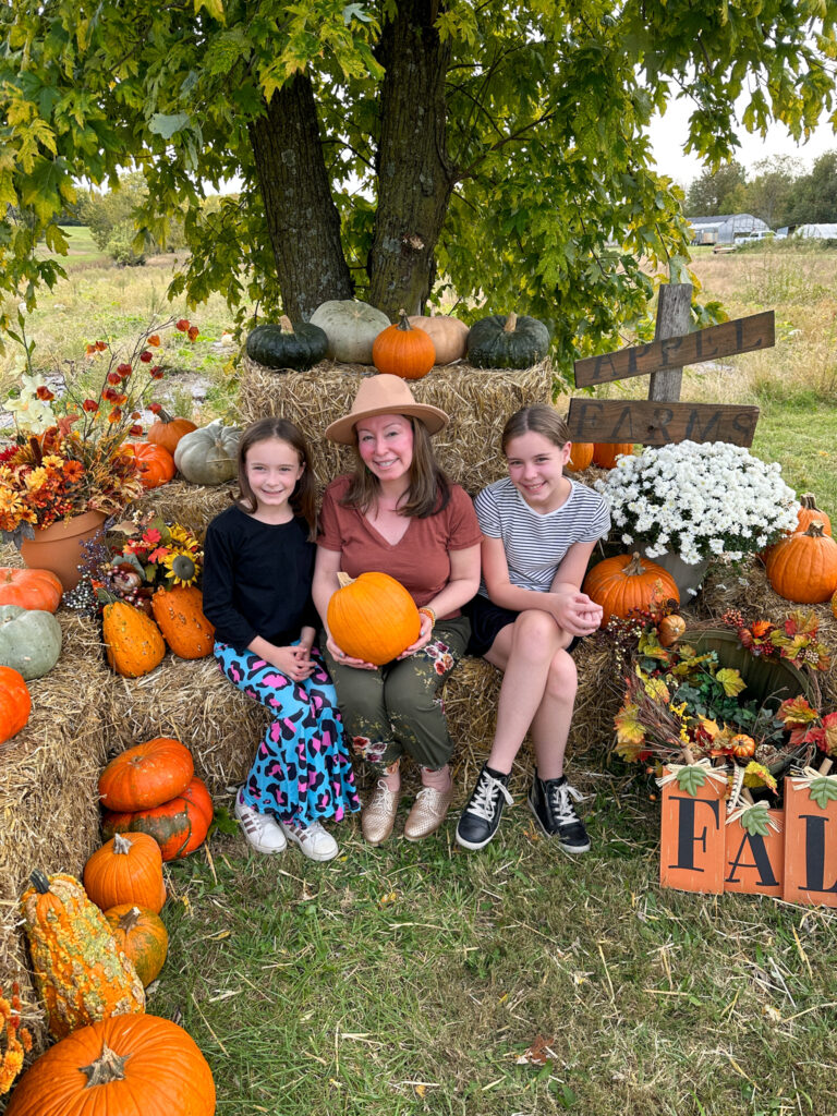 Arkansas lifestyle bloggers, Norah, Amy, and Harper pose with pumpkins at Appel Farms in Springdale