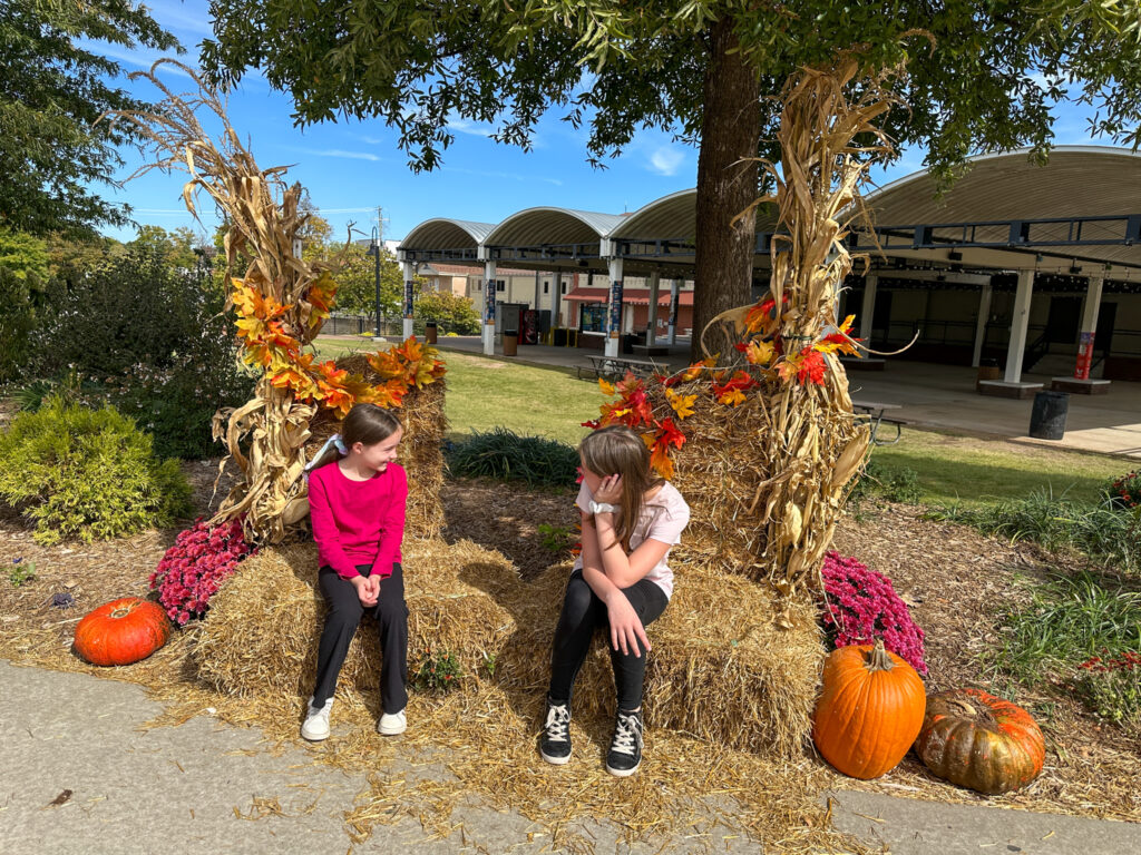 two girls sitting amongst pumpkins and mums in Shiloh Square