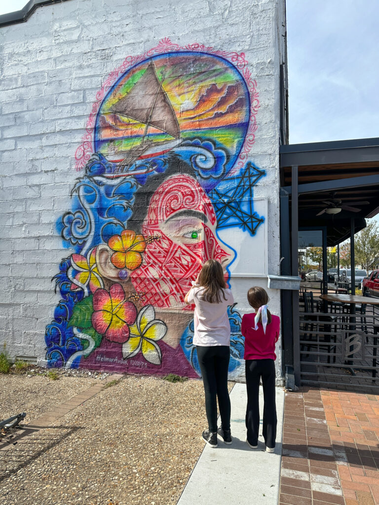 kid Arkansas lifestyle bloggers stand in front of large mural in downtown Springdale