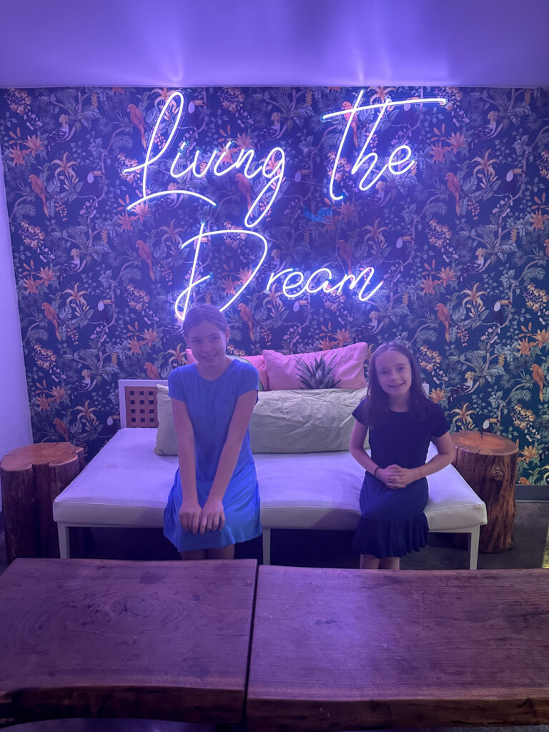 girls sit in front of Living the Dream sign at Con Quesos in northwest Arkansas