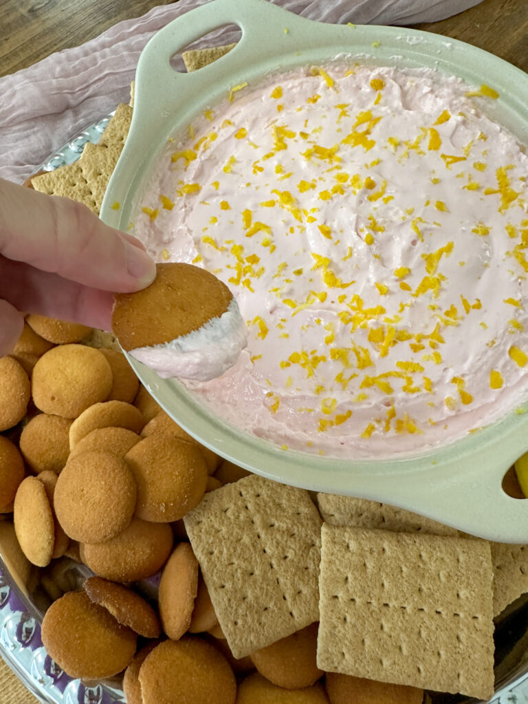 someone scoops pink lemonade dip on vanilla wafer over serving tray