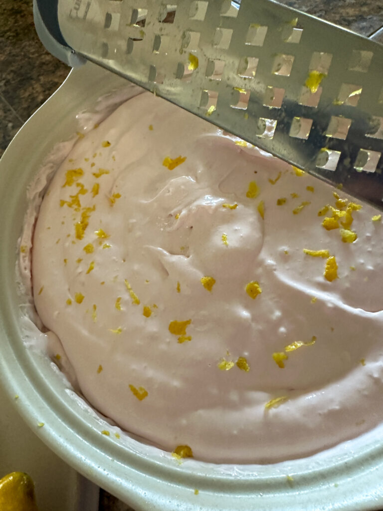 lemon zest falling from a lemon peeler on top of pink lemonade dip